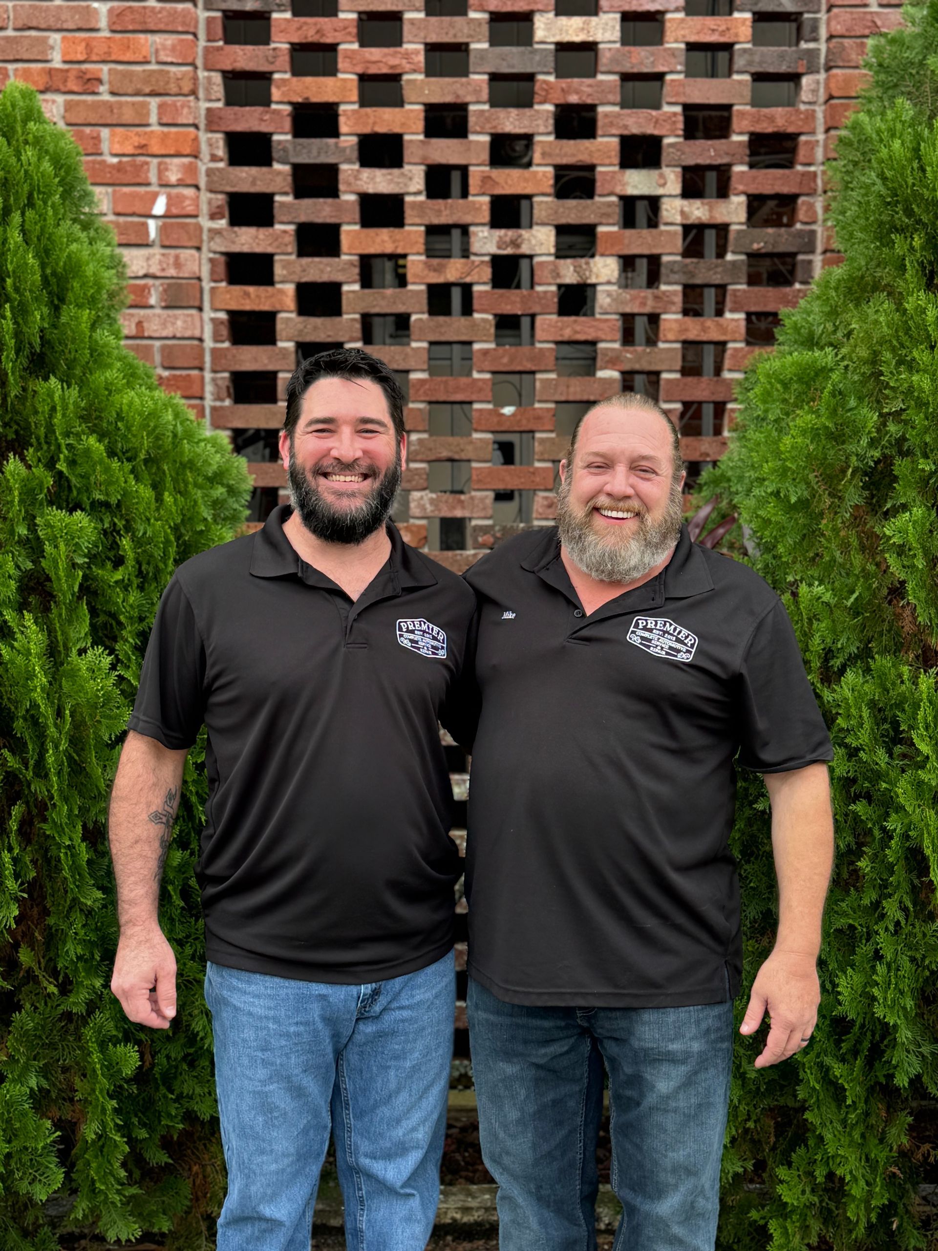 Two men are standing next to each other in front of a brick wall.