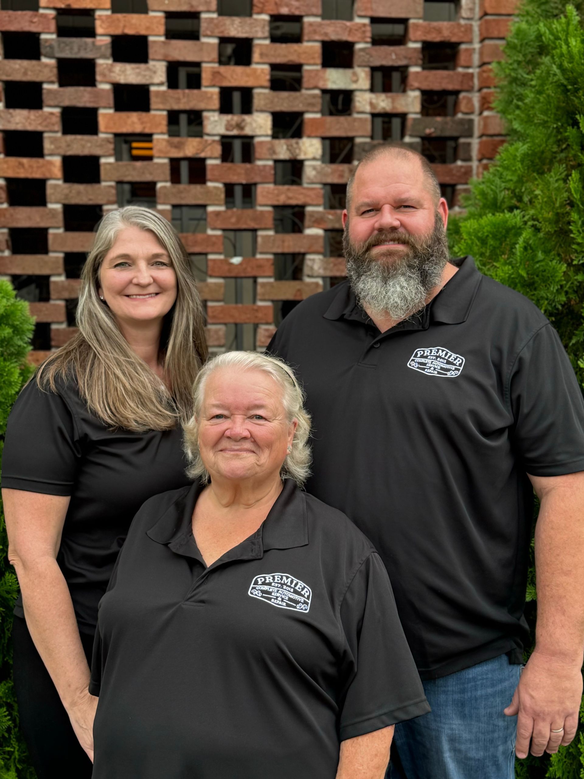 A man and two women are posing for a picture in front of a brick wall.