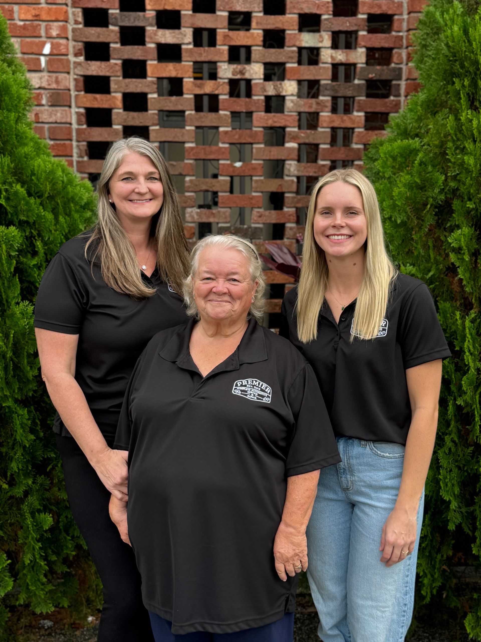 Three women are posing for a picture in front of a brick wall.
