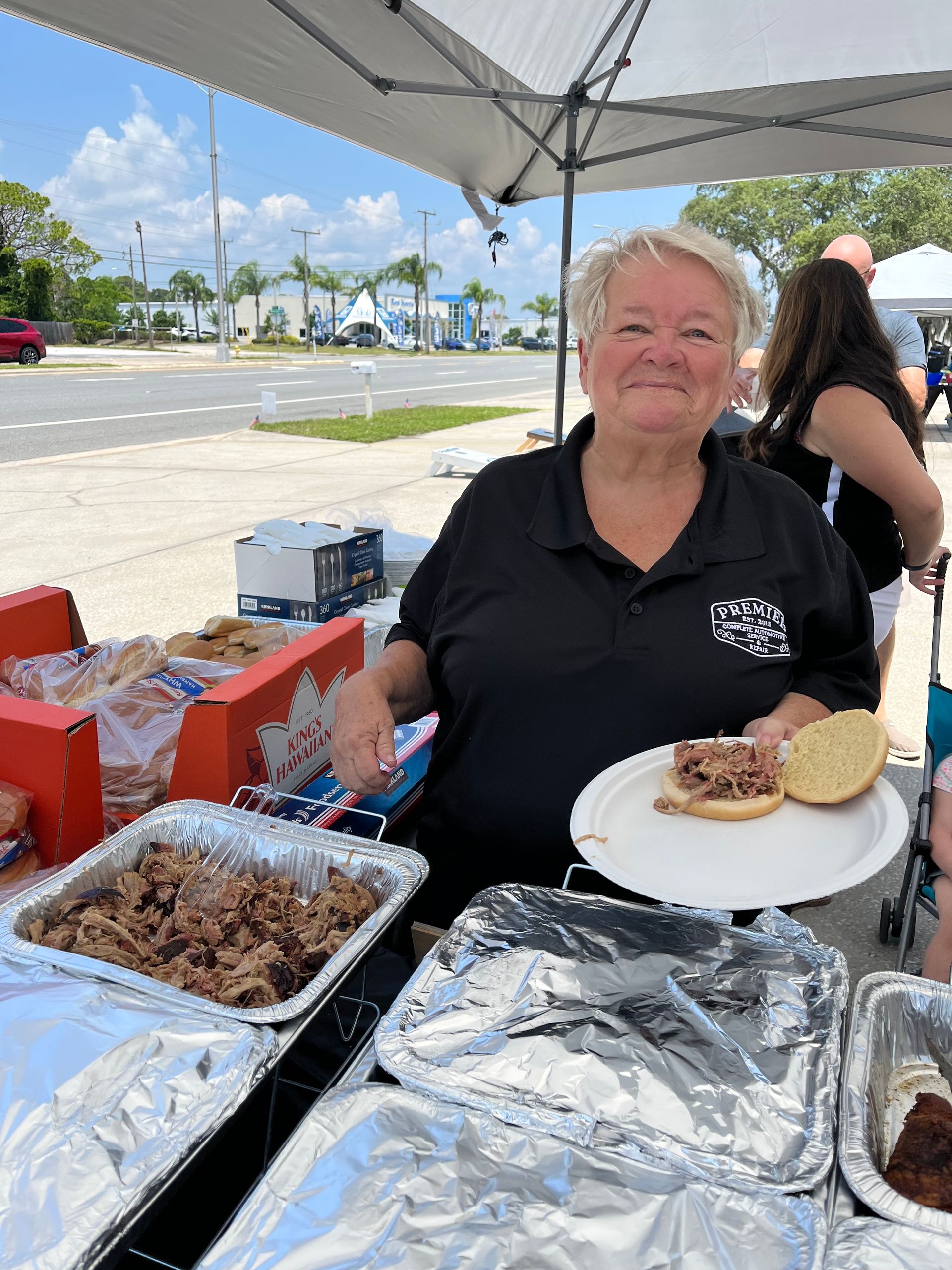A woman is standing behind a table holding a plate of food.