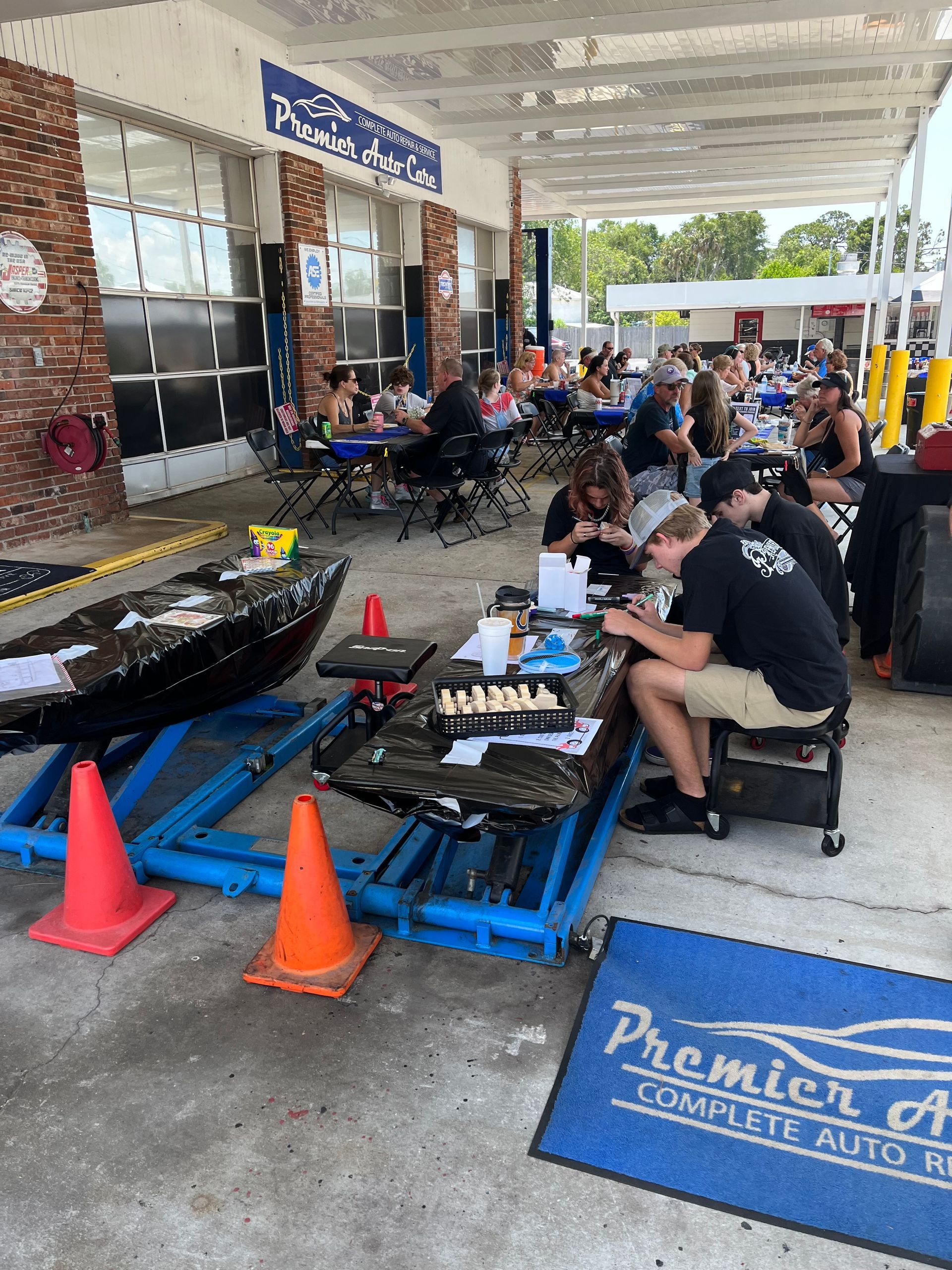 A group of people are sitting at tables outside of a car wash.