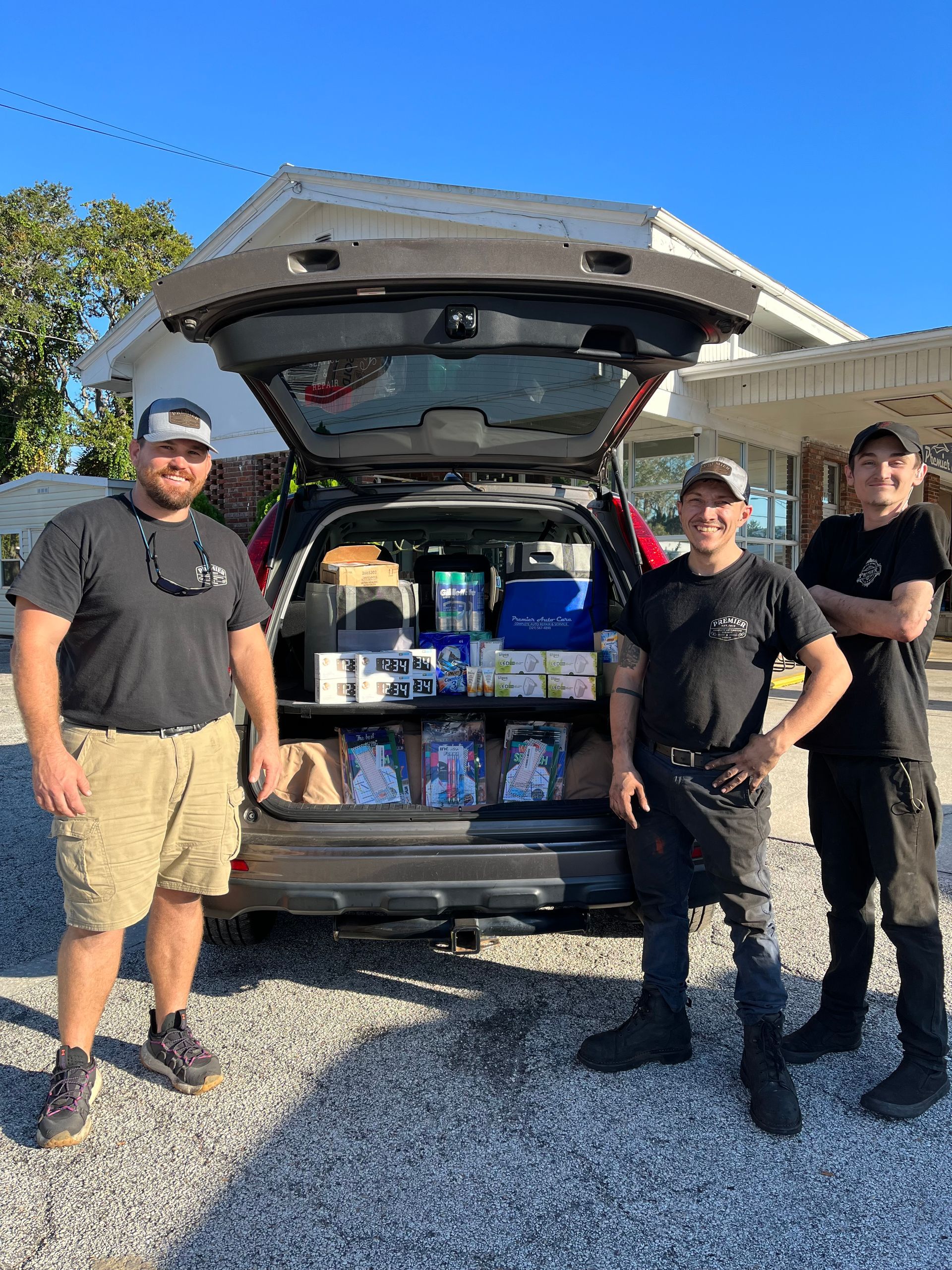 Three men are standing in front of a car with the trunk open.