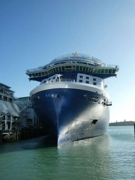 Blue cruise ship docked in harbor under a clear, blue sky.