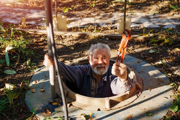 An elderly man with an adjustable wrench in the manhole of a water well. An elderly man with an adjustable wrench in the manhole of a water well.