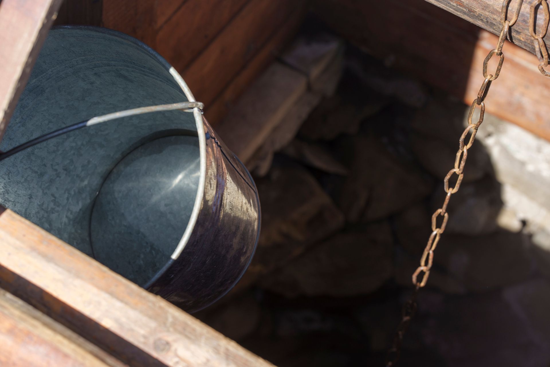 An antique water well with a metal bucket within it.