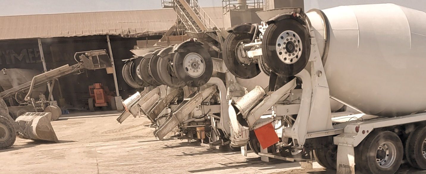 A row of concrete mixers are parked in a parking lot. A row of concrete mixers are parked in a parking lot.
