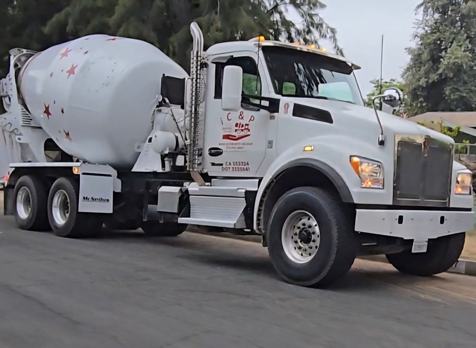 A red and white concrete mixer truck is parked in a dirt lot