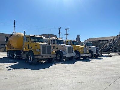 A row of concrete trucks are parked in a parking lot.