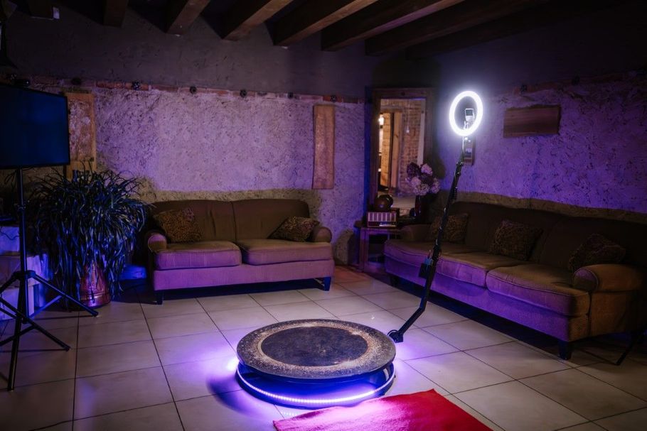 Purple-lit lounge with couches, tiled floor, ring light, and a low circular table on a rug.