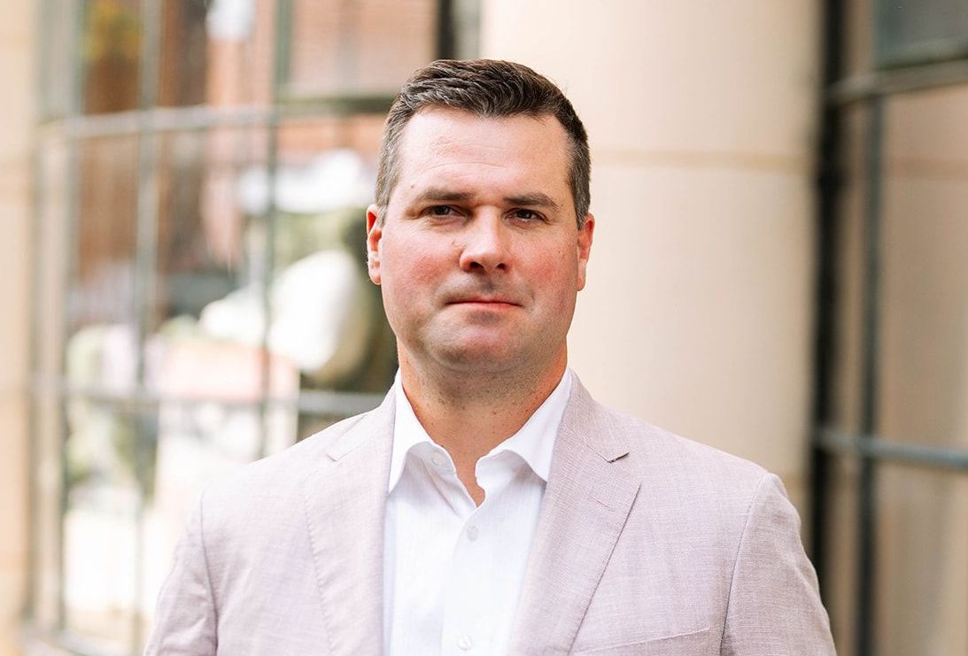 A man in a suit and white shirt is standing in front of a building.