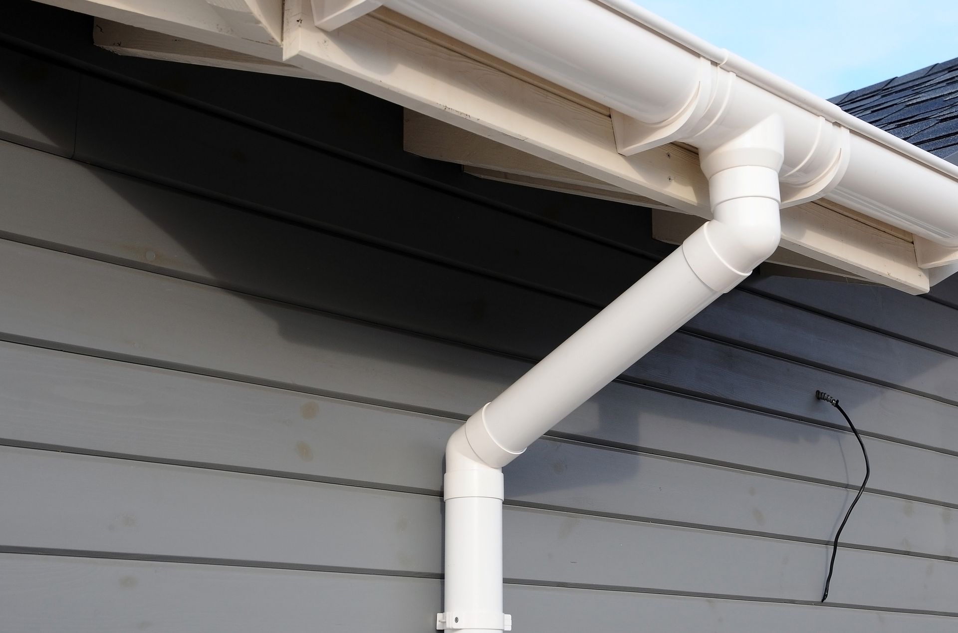 White rain gutter and downspout on a gray house, angled and connected.