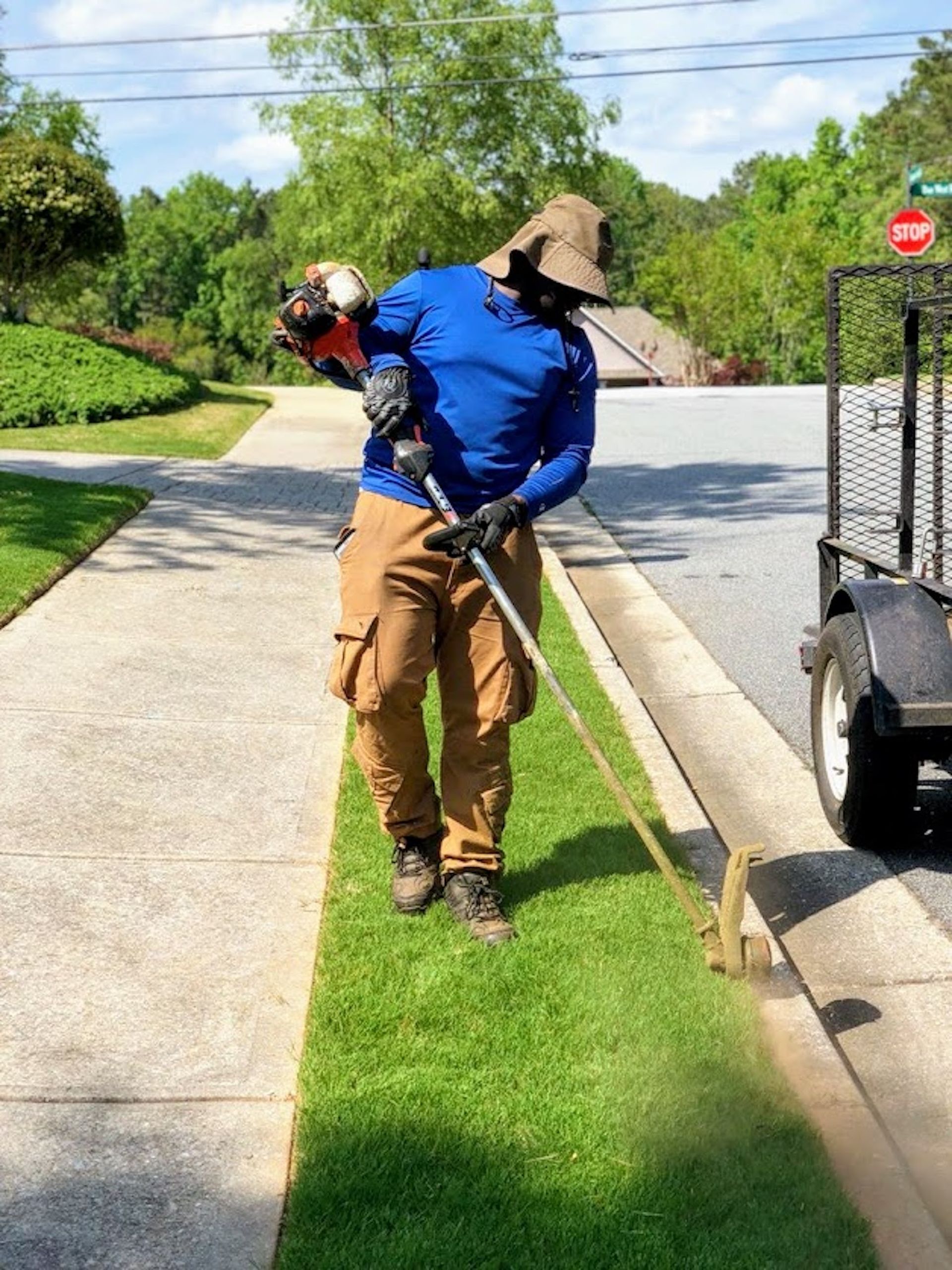 A man is standing on a sidewalk cutting grass with a lawn mower