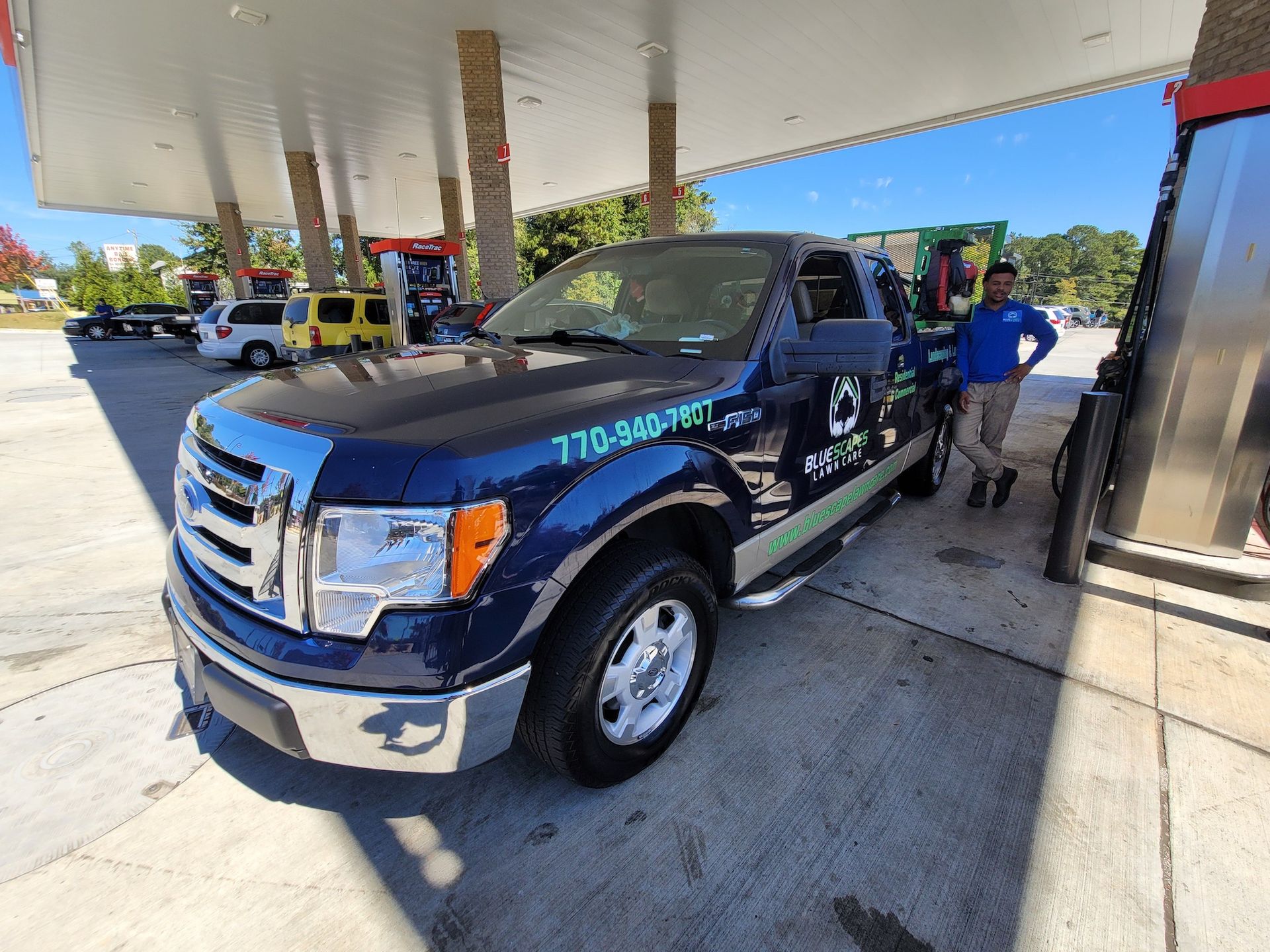 A man is standing next to a blue truck at a gas station