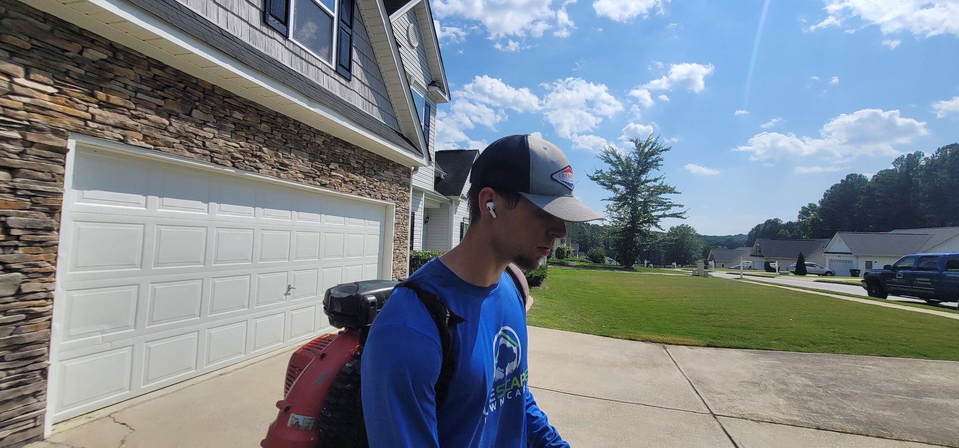 A man with a backpack is walking down a sidewalk in front of a house