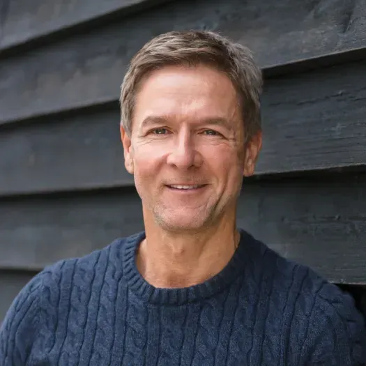 The man is wearing a blue sweater and smiling for the camera.