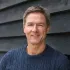 The man is wearing a blue sweater and smiling for the camera.