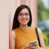 A woman wearing glasses is leaning against a wall while holding a cell phone.