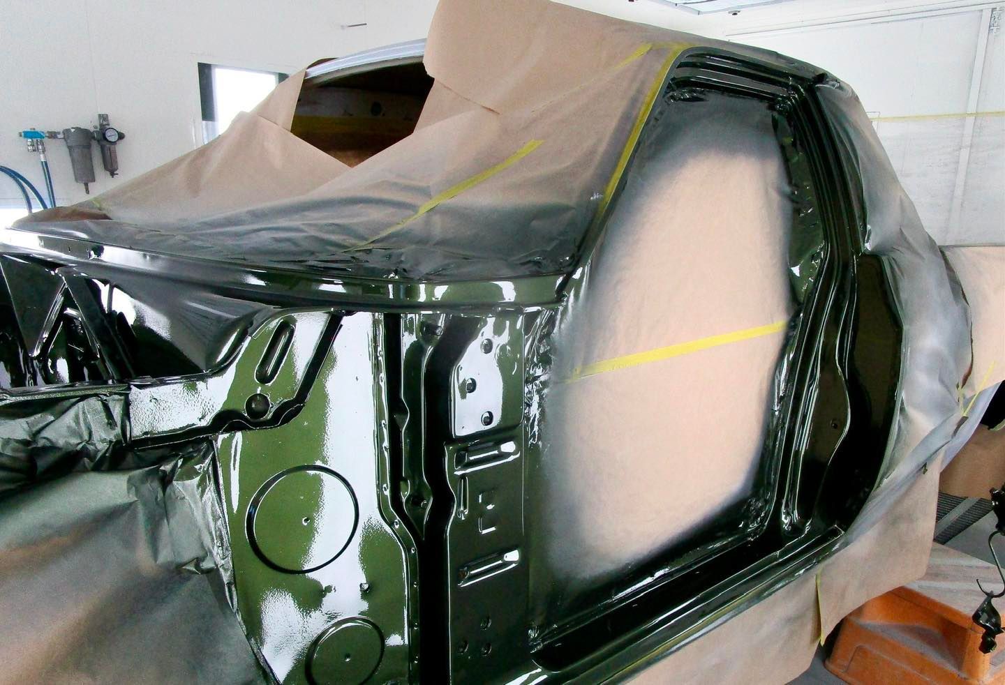 Car frame freshly painted green in a workshop, masked for further painting.