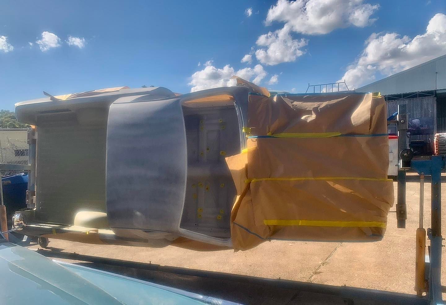 Stacks of wood pallets wrapped in yellow tarps outdoors under a blue sky.
