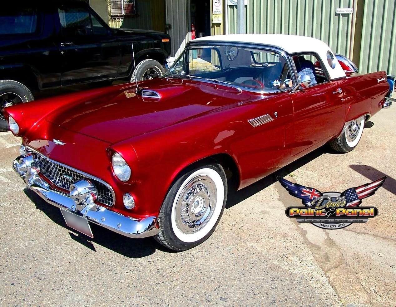 Black classic Mini car parked outside a workshop with a red Mustang.
