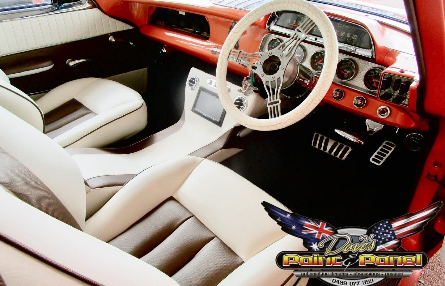 Interior of a classic red car with cream and gray seats, white steering wheel, and silver accents.
