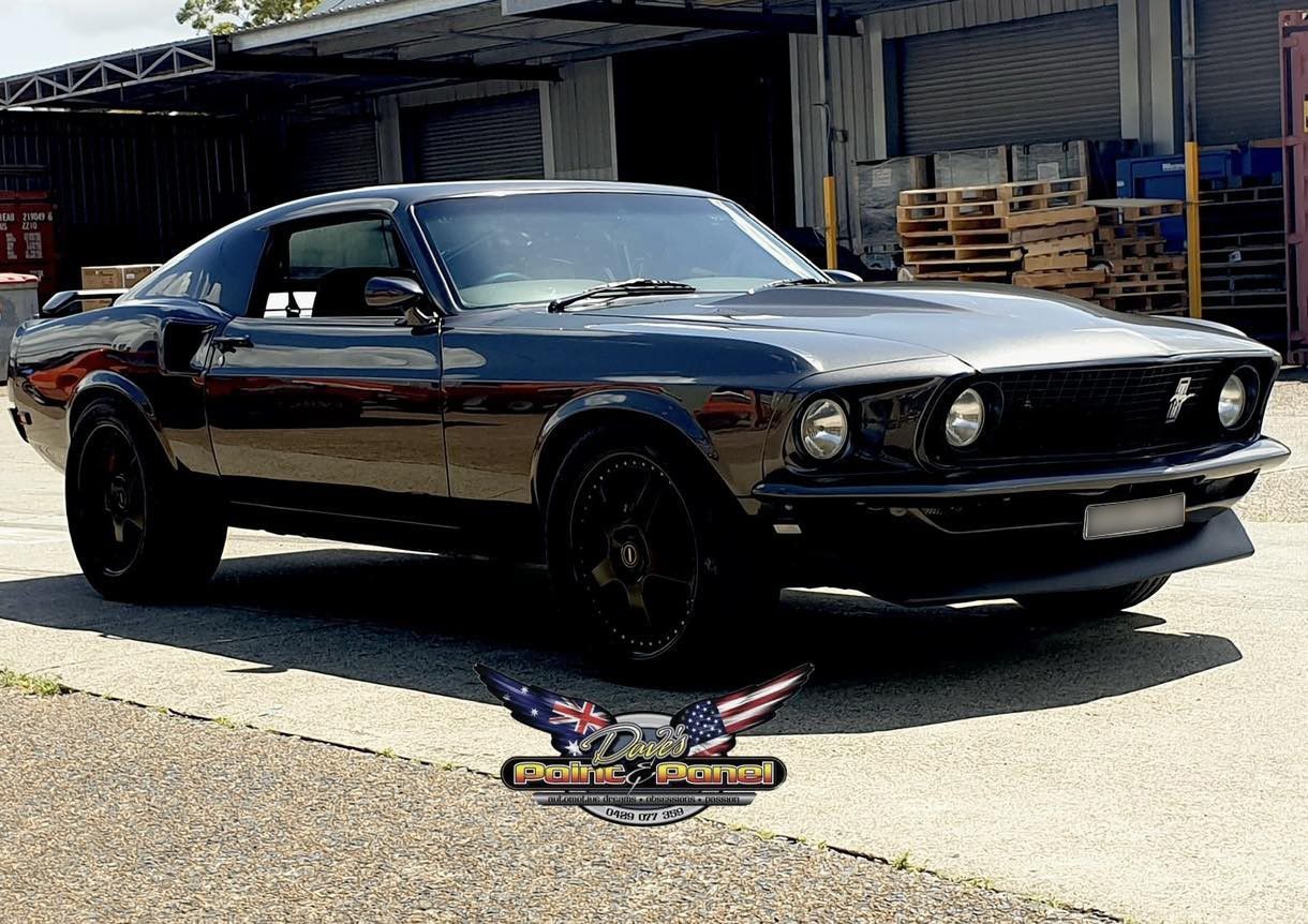 Black classic Mustang with a custom design parked in front of a loading dock.