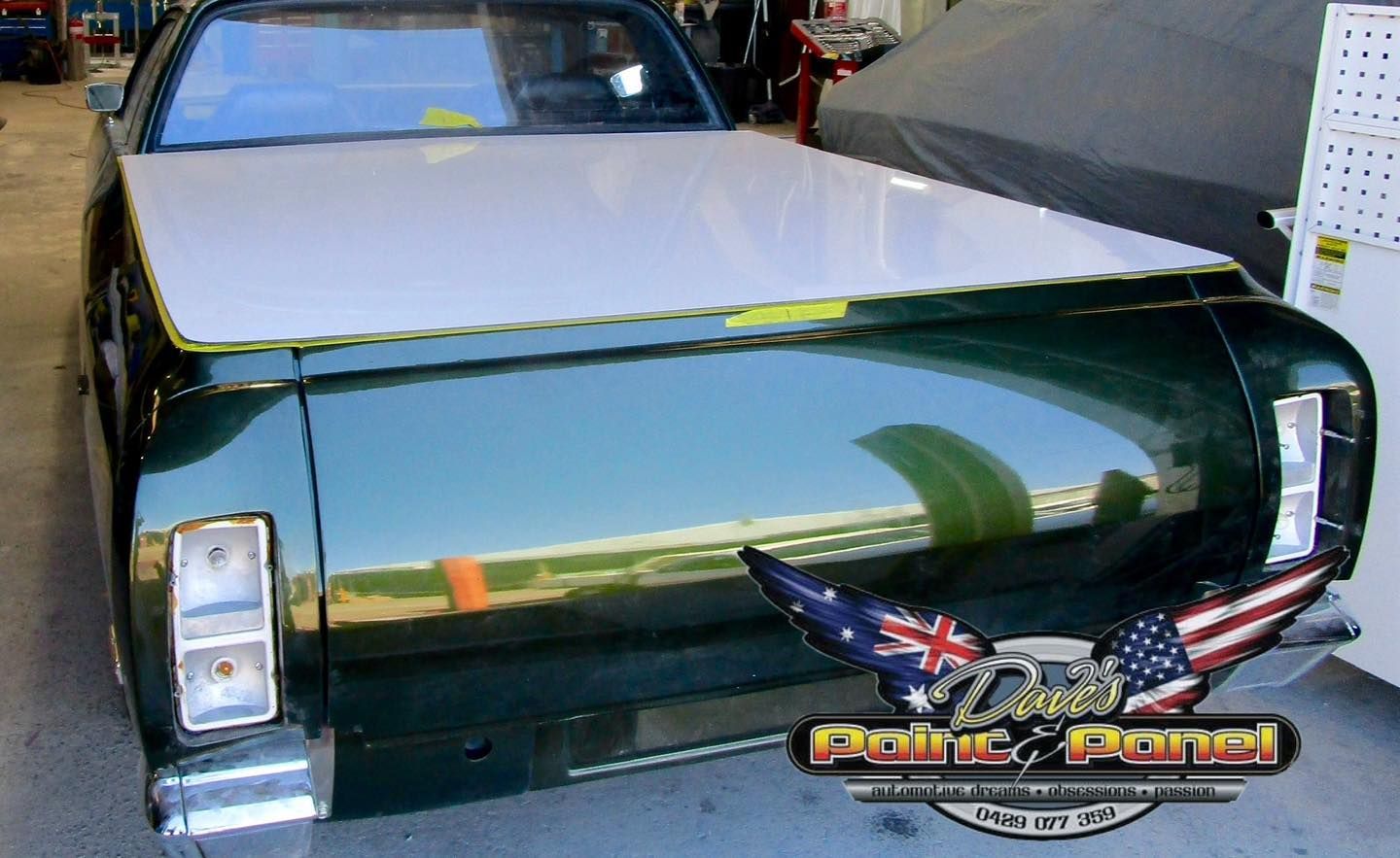 Dark green classic car with a white hood in a garage.
