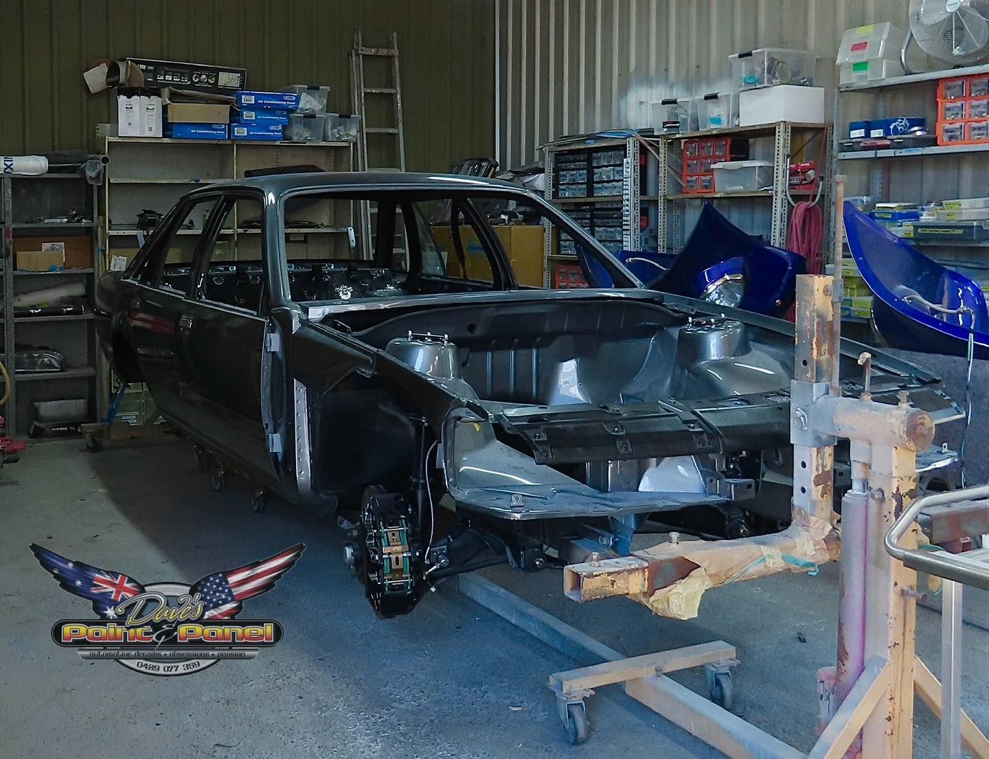 Black car in a workshop, stripped down for restoration, with parts and tools in the background.