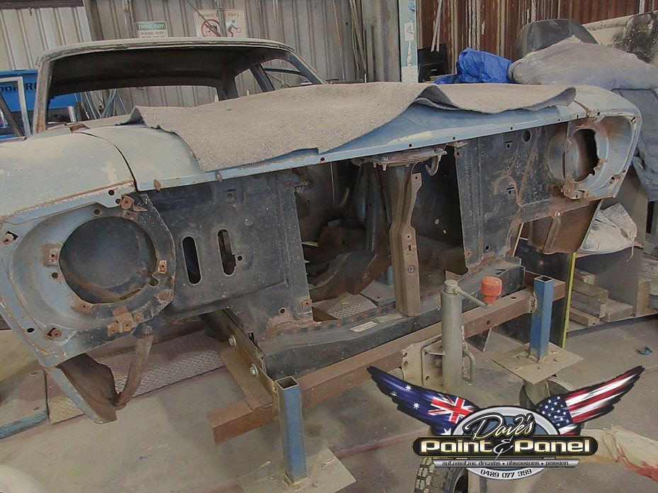 Partially disassembled classic car in a workshop, with rust and preparation for restoration.