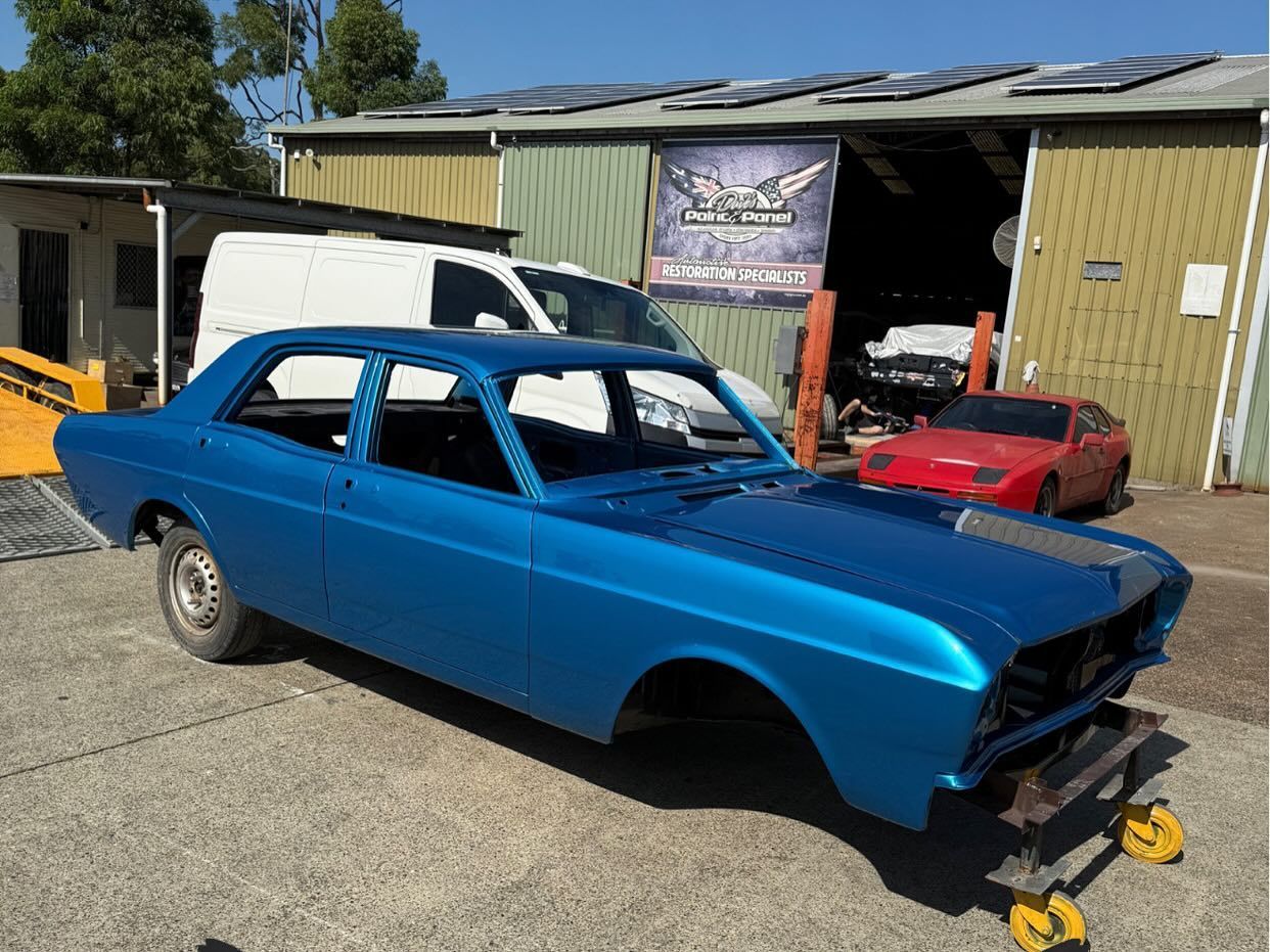 Blue classic car body in a garage setting, awaiting restoration.