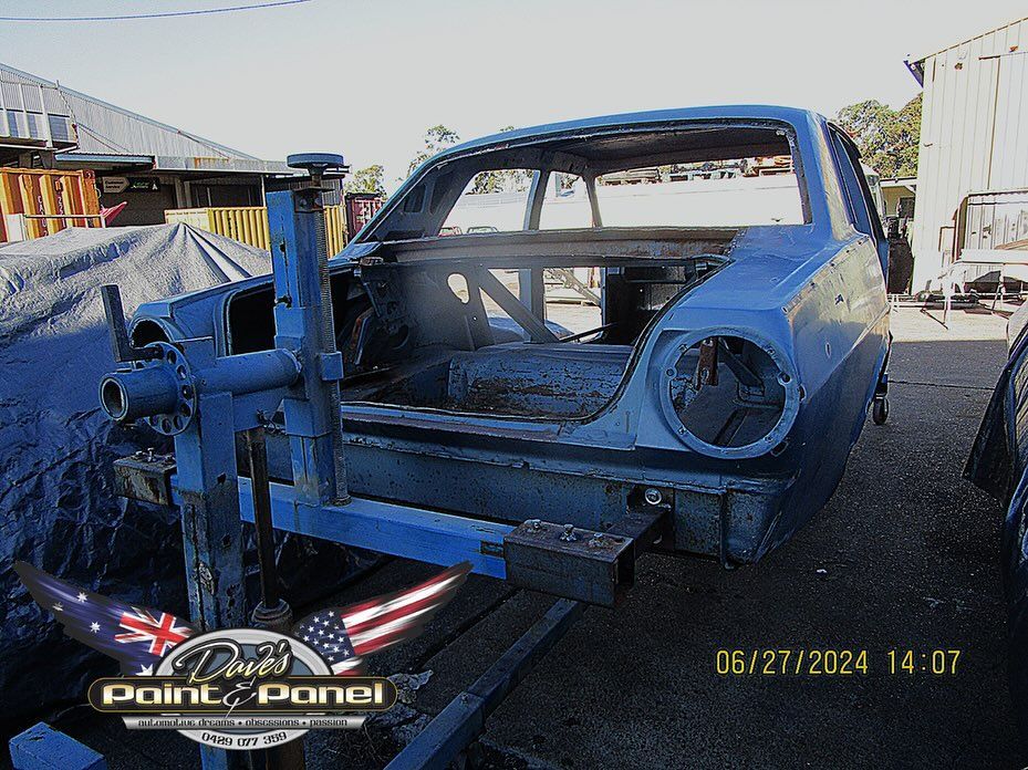 Blue car frame mounted on a blue rotisserie outdoors, likely for restoration work.