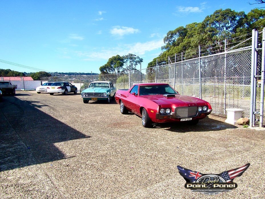 Black Mini Cooper with trailer parked outside a garage on a sunny day.