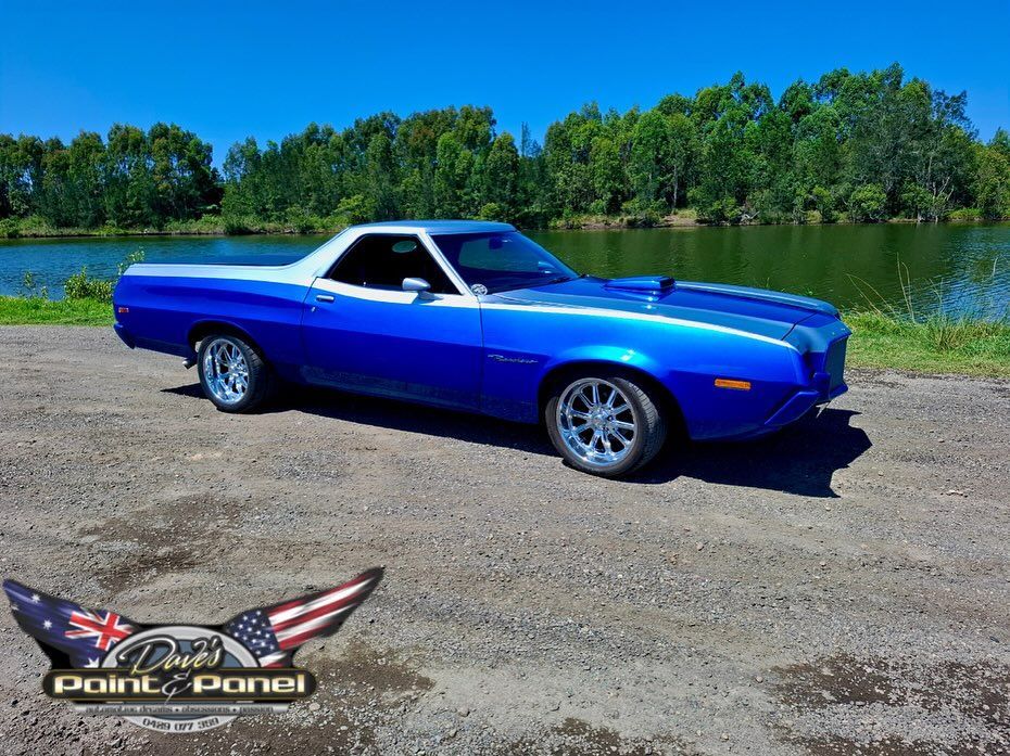 Blue and silver vintage Ford Torino Ranchero parked by a lake on a sunny day.