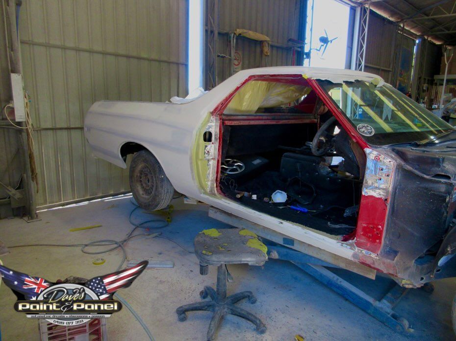 A red and white classic El Camino in a garage, undergoing restoration with open doors.