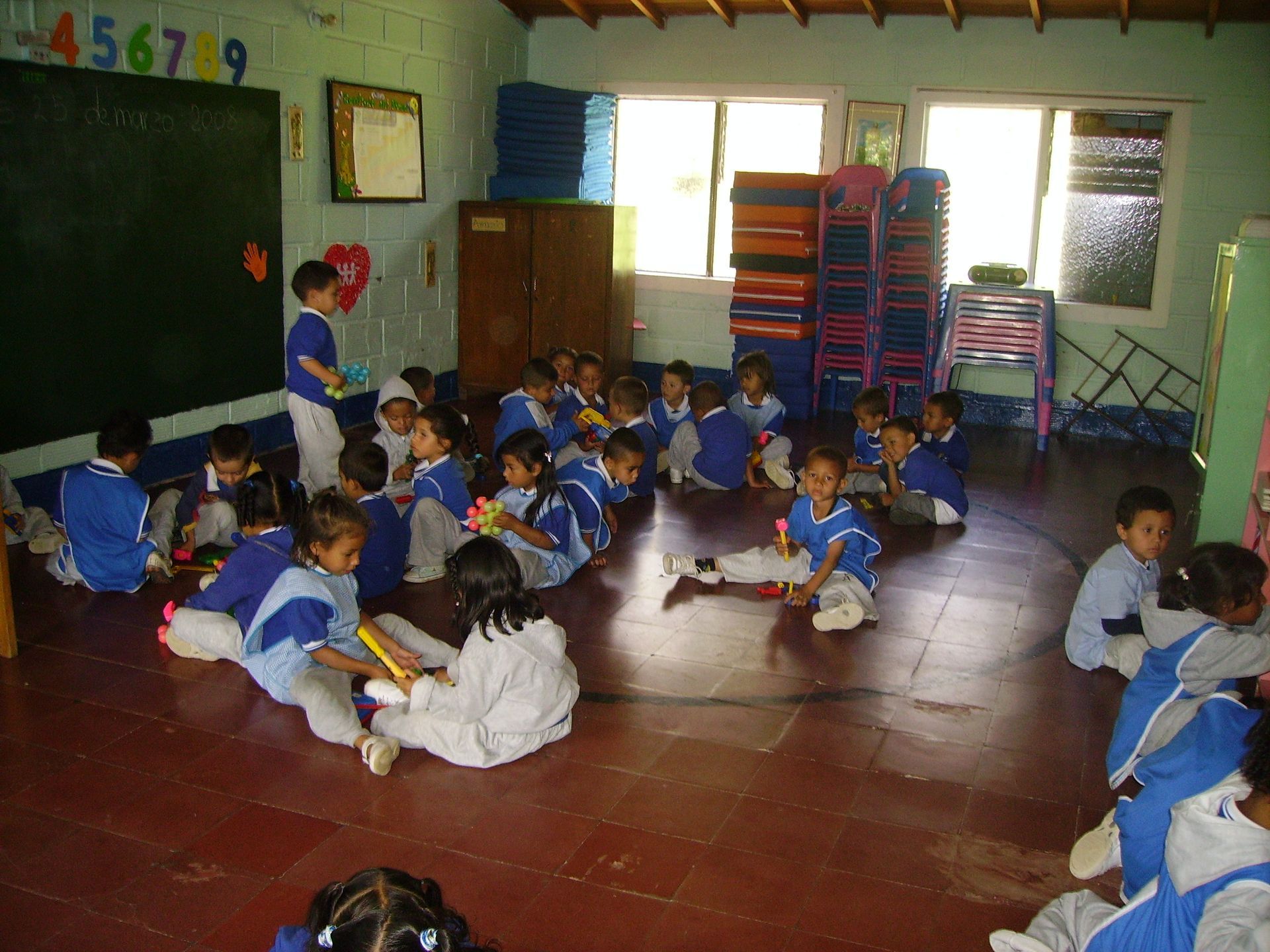 I bambini in uniforme blu sono seduti sul pavimento di un'aula e giocano con i giocattoli.