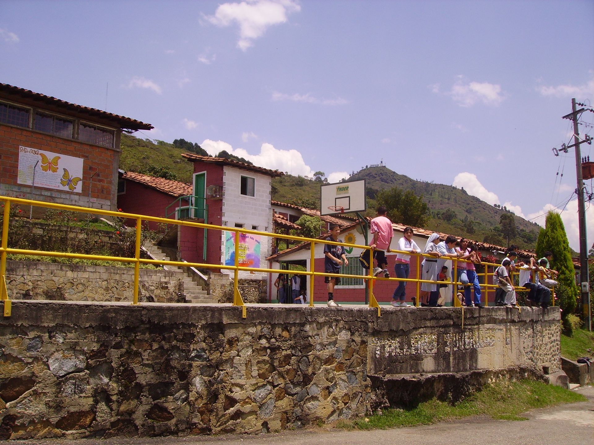 Edificio scolastico con bambini sul balcone, montagne sullo sfondo, giornata di sole.