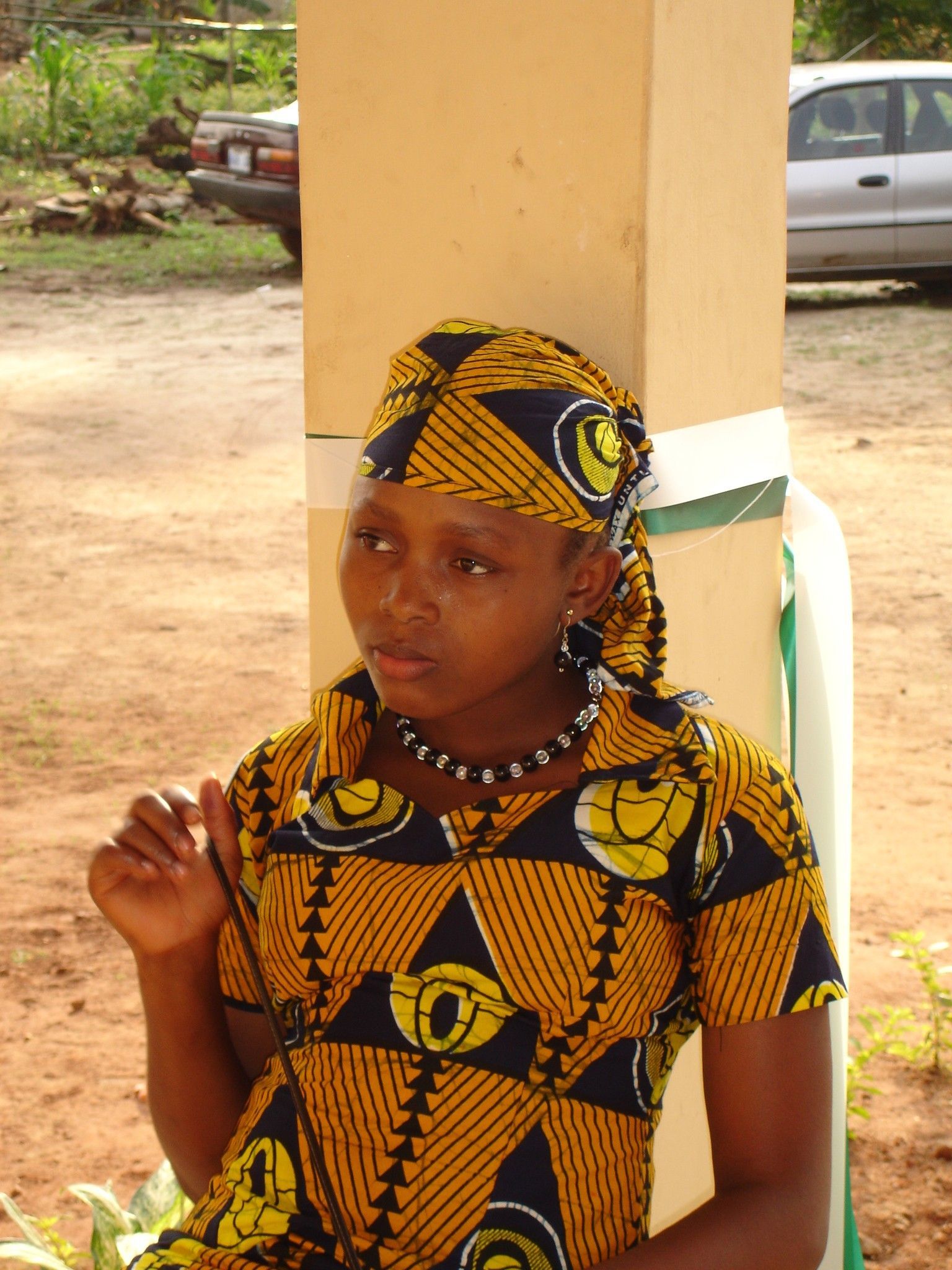 Donna vestita con abiti a fantasia gialla e nera, seduta all'aperto, con lo sguardo rivolto di lato.