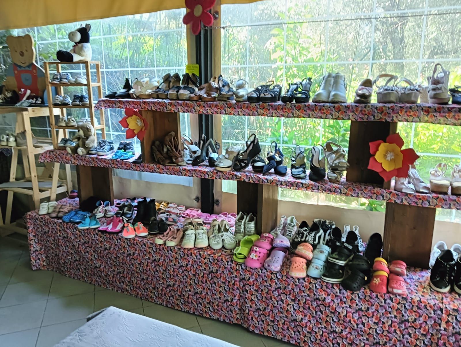 Scarpe esposte su scaffali a più livelli con una base colorata e strutturata, accanto a una finestra.