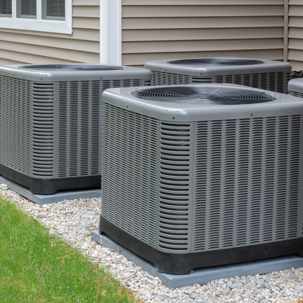 Three air conditioners are sitting on the side of a house.