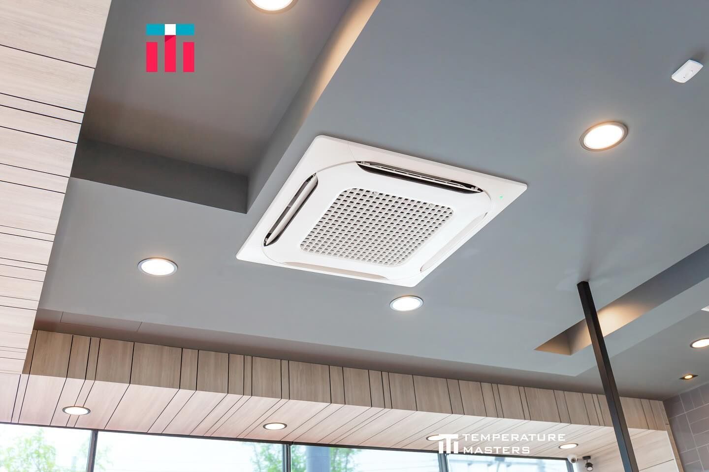 A square air conditioner is hanging from the ceiling of a room.