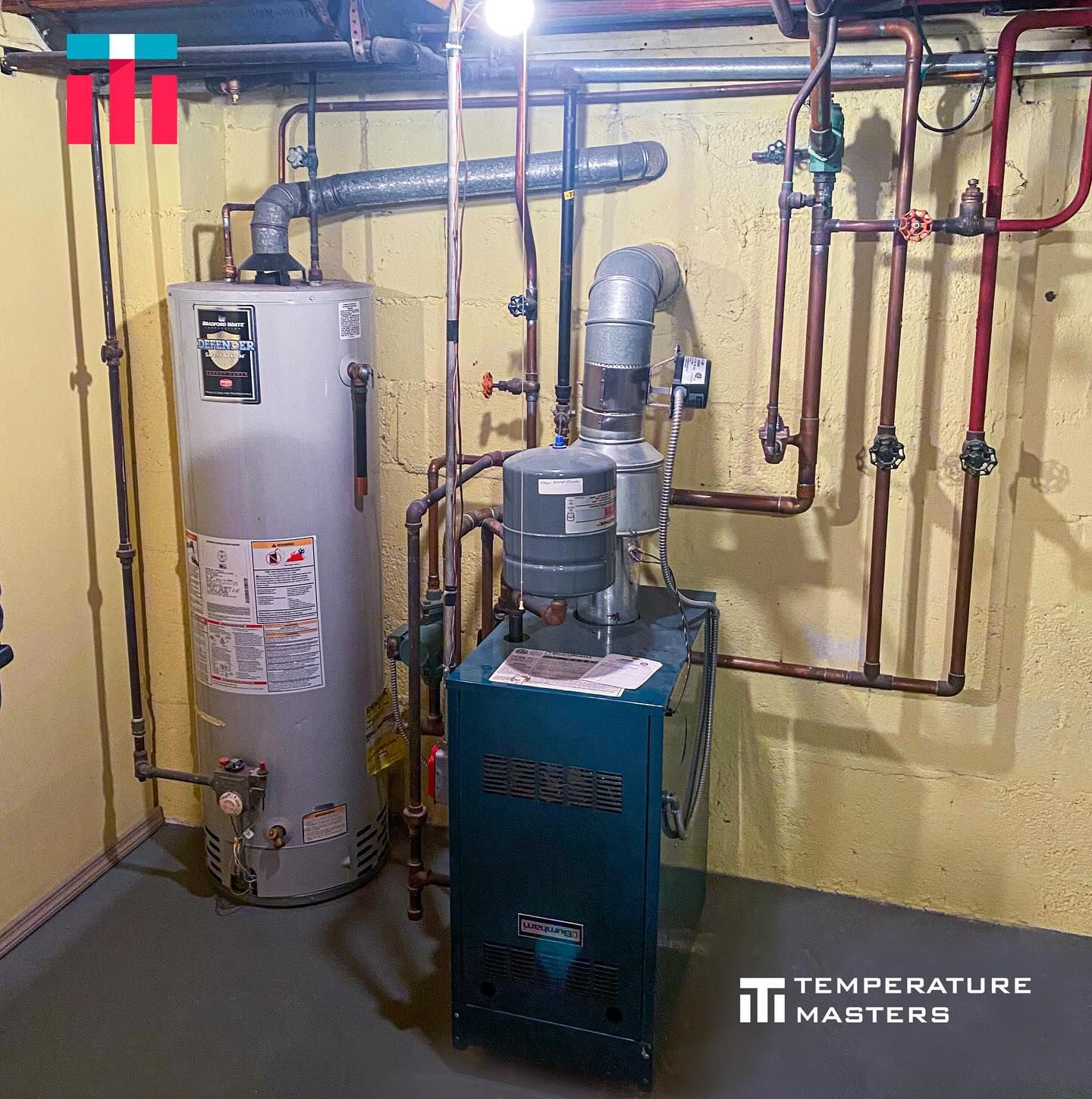A water heater is sitting next to a boiler in a basement.