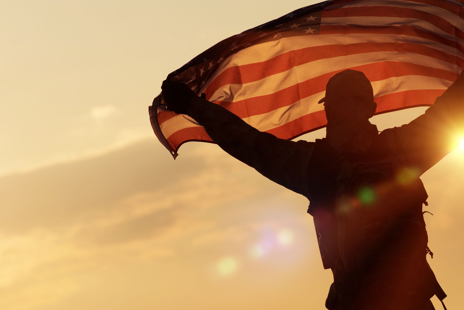 A silhouette of a man holding an american flag at sunset.