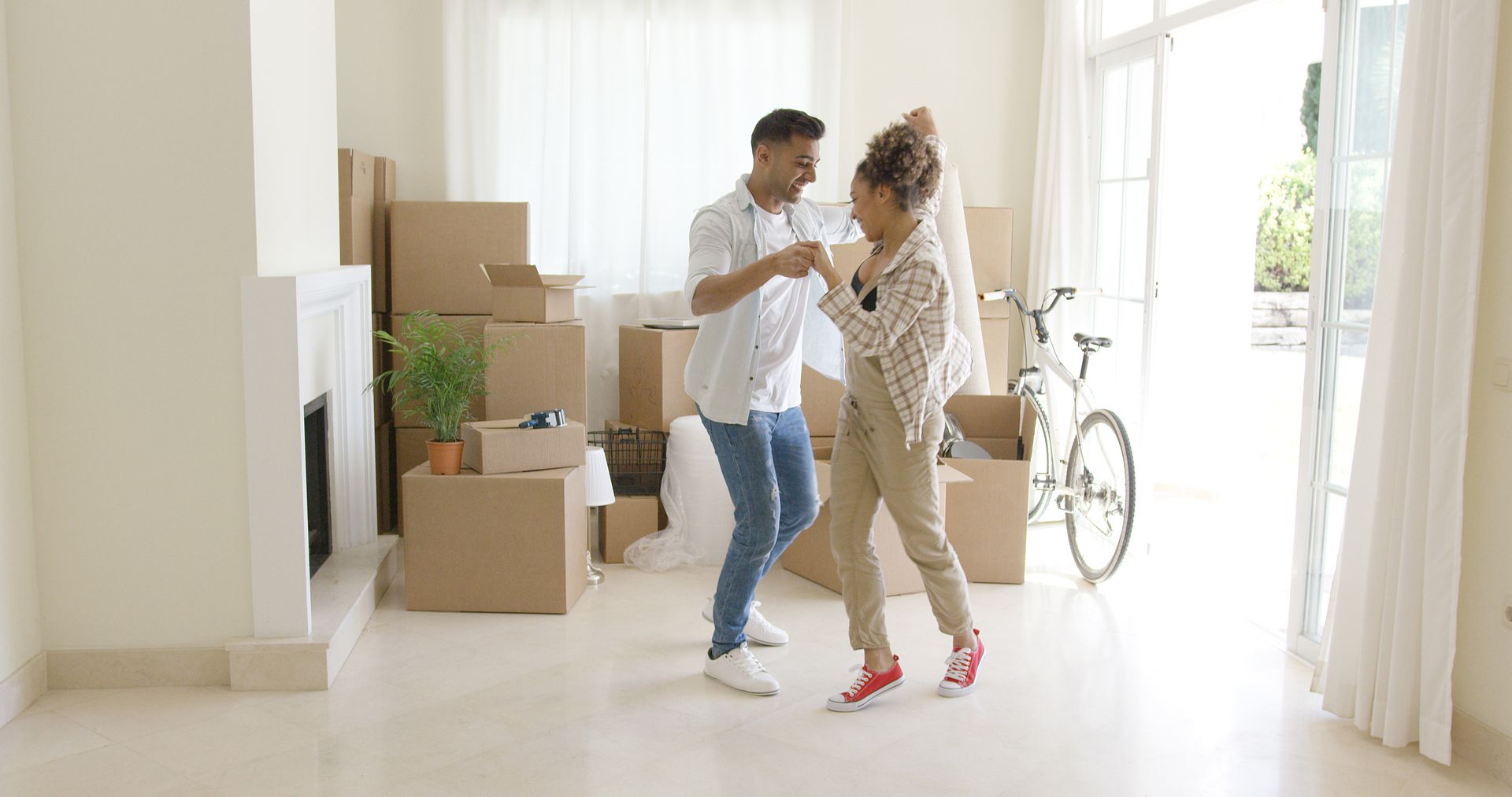 A man and a woman are dancing in a living room filled with cardboard boxes.