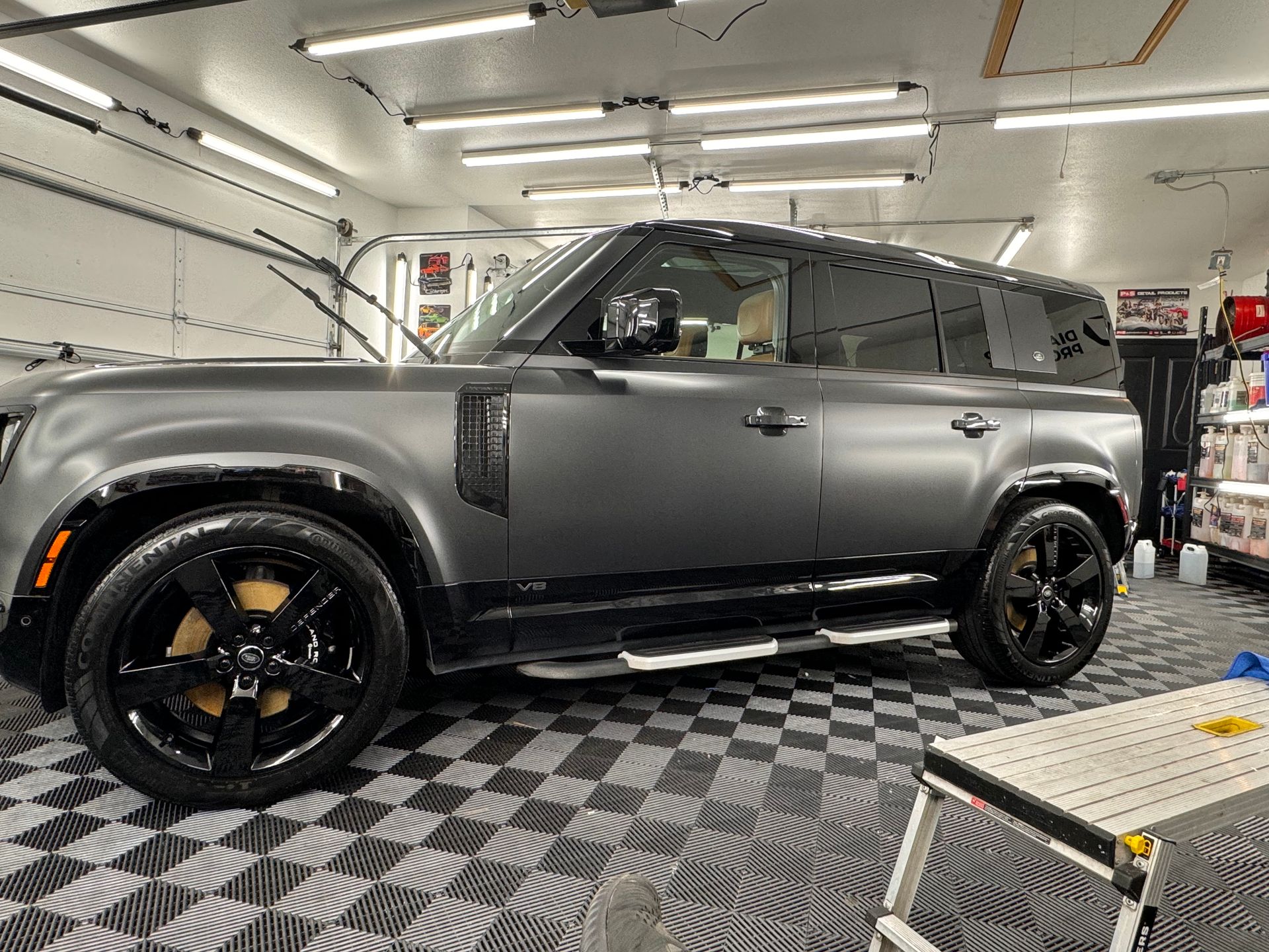 A black land rover defender is parked in a garage.