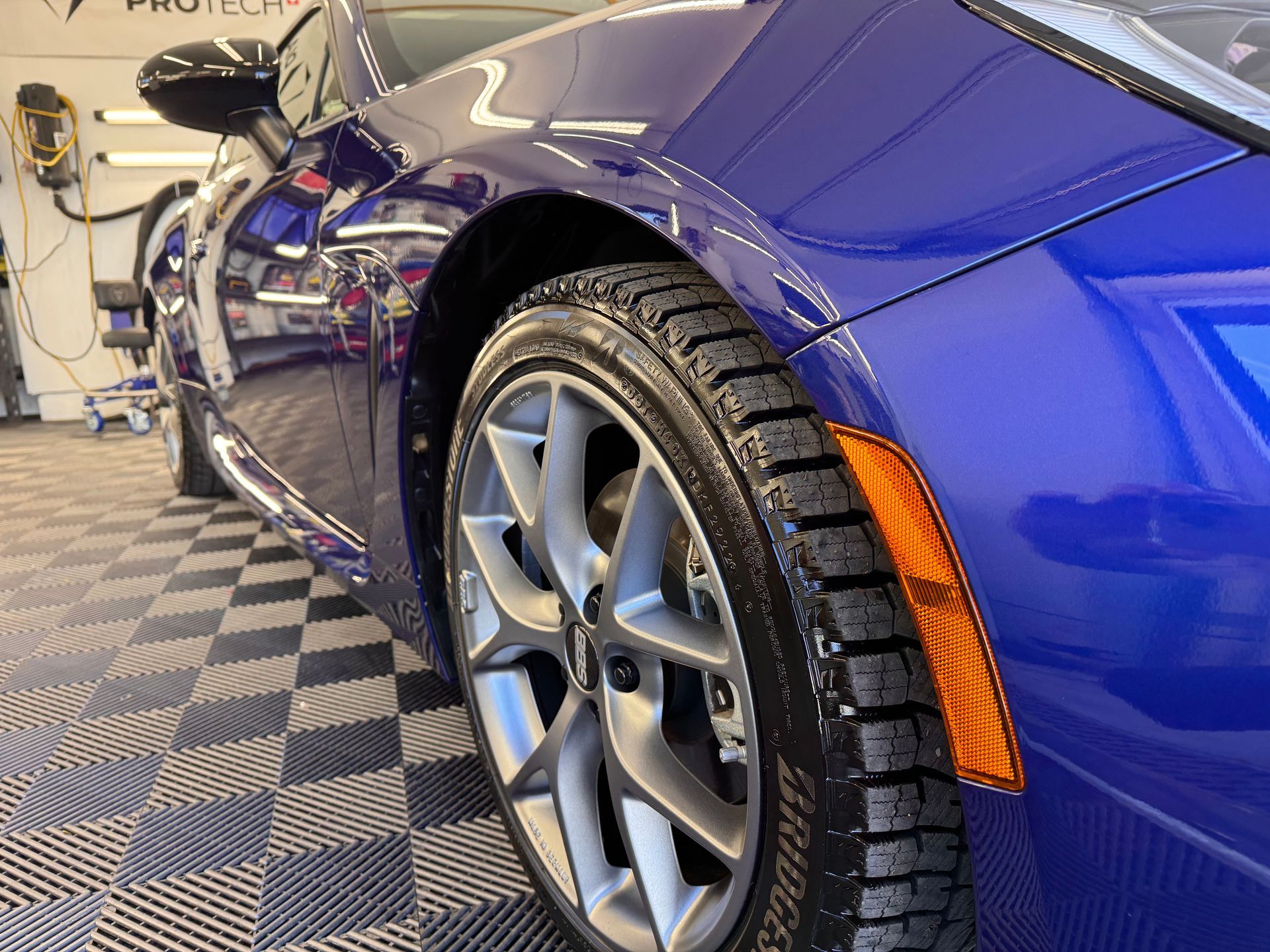 A blue sports car is parked on a checkered floor in a garage.