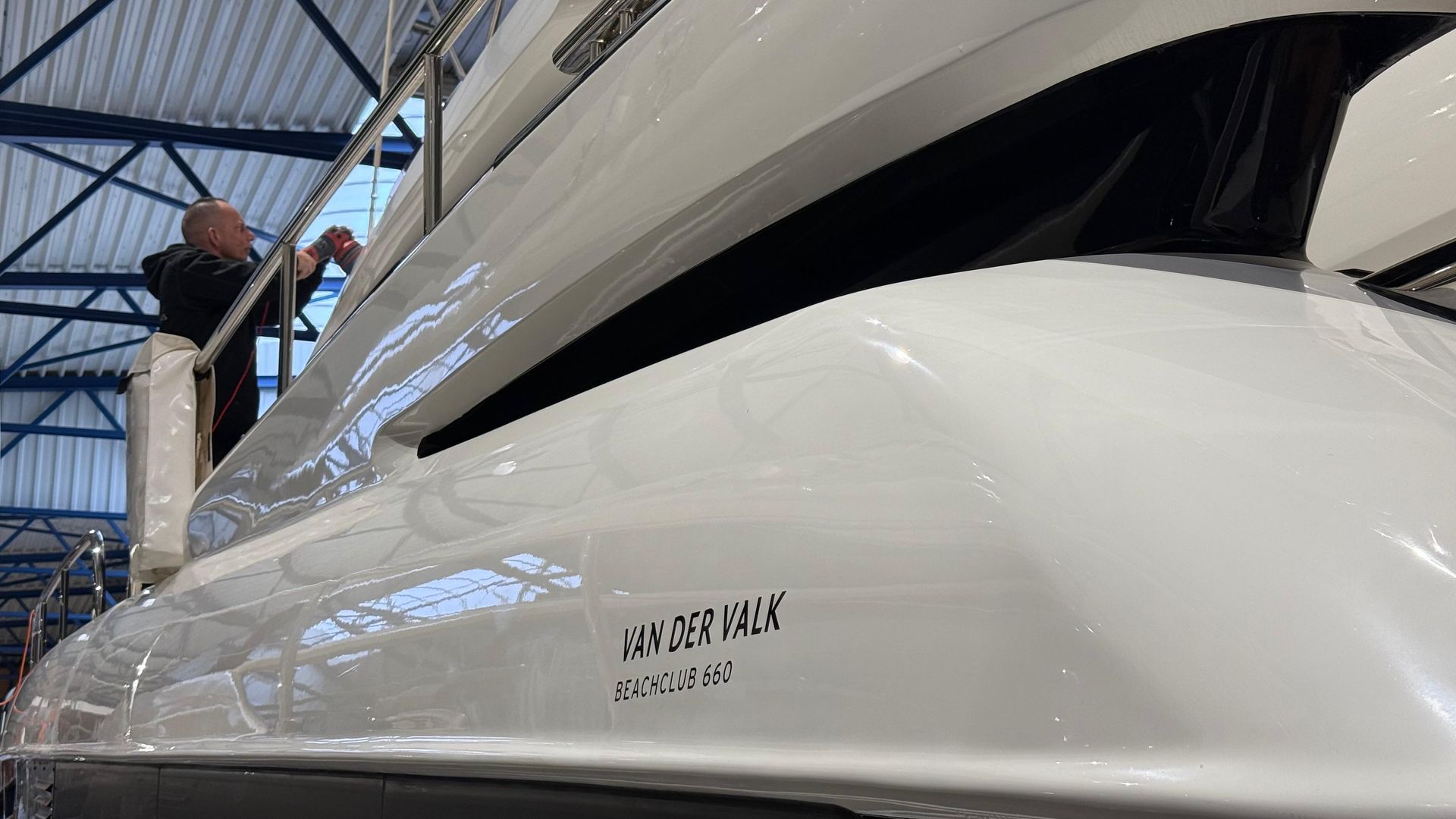 Een man werkt aan een witte boot in een pakhuis.