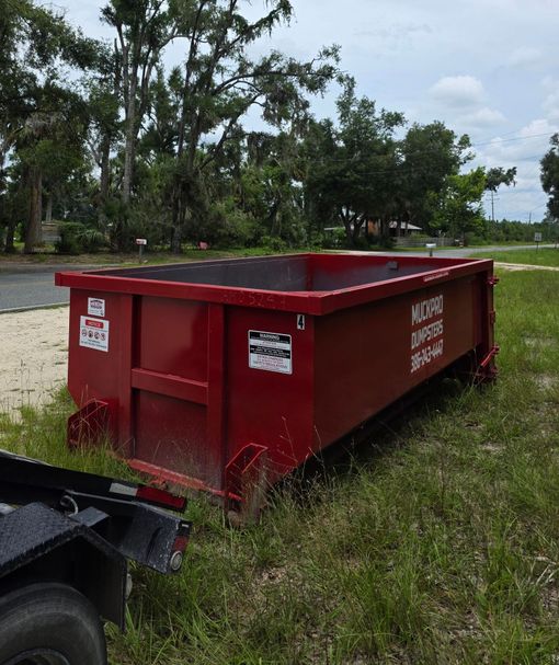 A red muckpro dumpster sits in front of a house in Live Oak, Florida