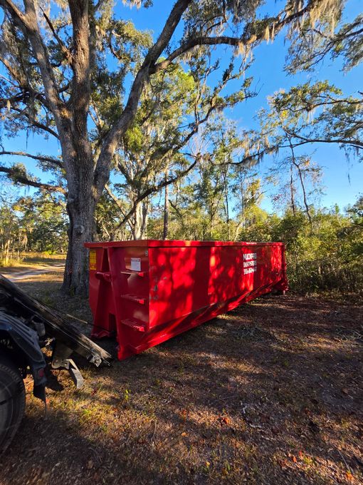 A red muckpro dumpster sits in front of a house in Live Oak, Florida