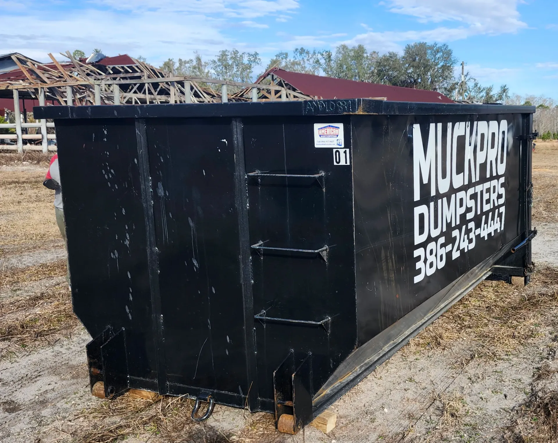 A large black dumpster is sitting in the middle of a field.