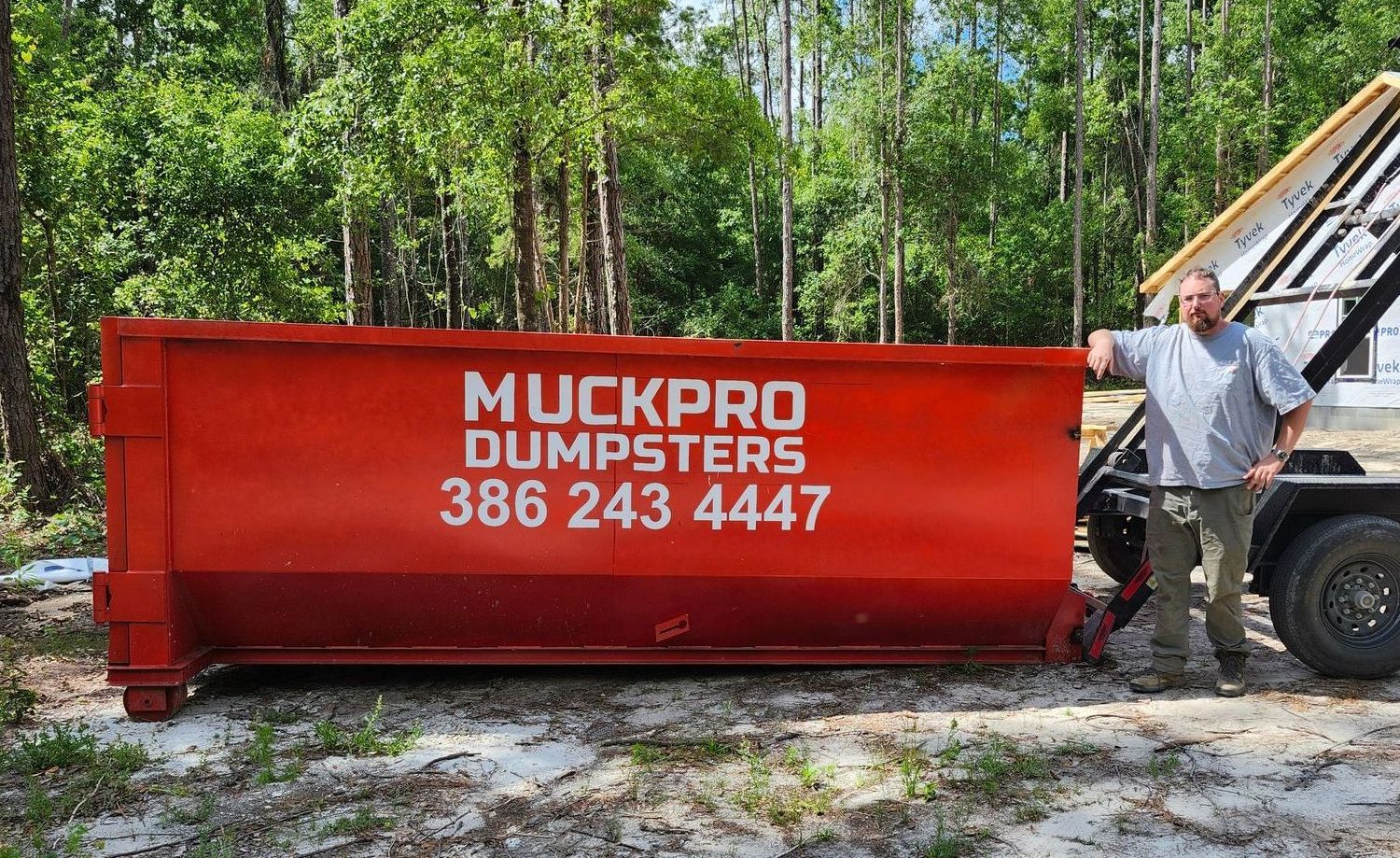 A red muckpro dumpster sits in front of a house in Live Oak, Florida